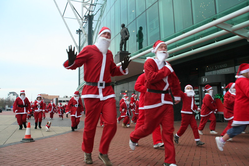 Group of people dressed as Santa running on a city sidewalk